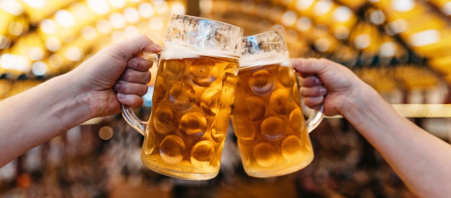 Zwei Personen stoßen in einem Festzelt mit zwei Maßkrügen an und prosten sich zu.