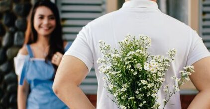 Mann steht vor Frau und versteckt Blumen für sie hinter seinem Rücken