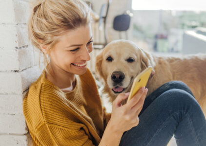 Frau mit Hund schaut lachend aufs Handy